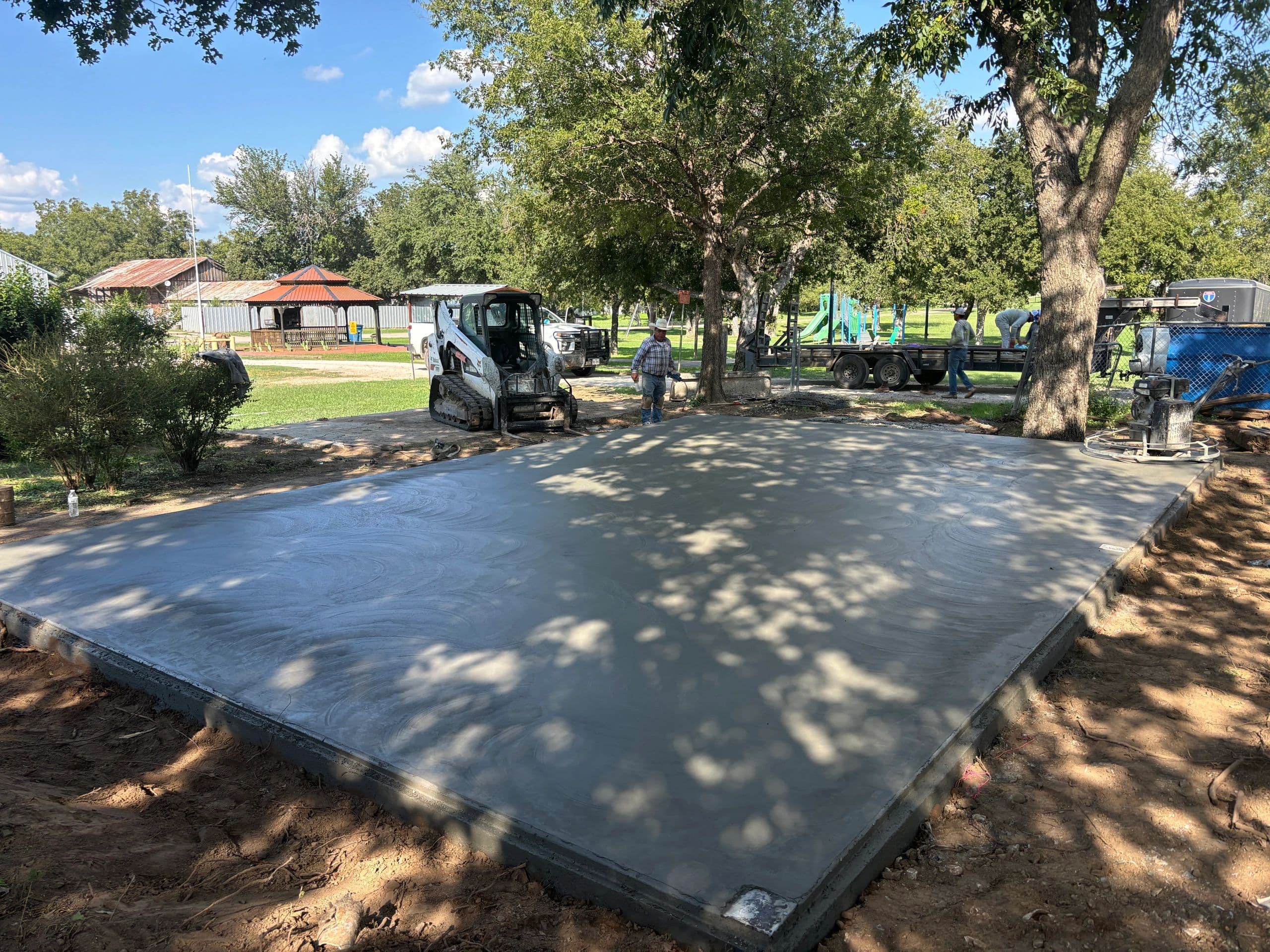Commercial concrete flatwork slab with skid steer, shaded lot